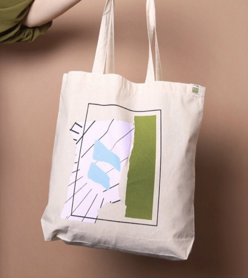 Someone's arm holding out a canvas tote with an abstract design printed on the front